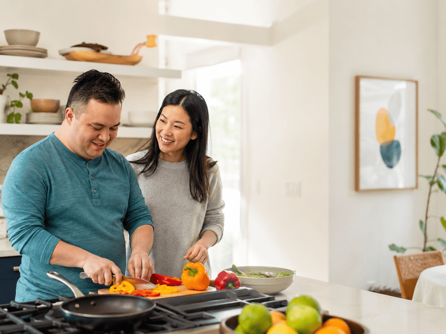 An adult cuts fresh vegetables at the kitchen island in their own home, with a support person alongside.